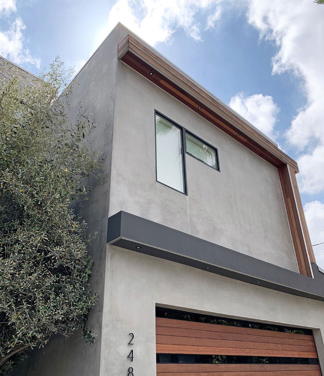 A photograph of an exterior facade of the home chosen for the event venue. The facade is cement and square with decorative wooden and steel beams.